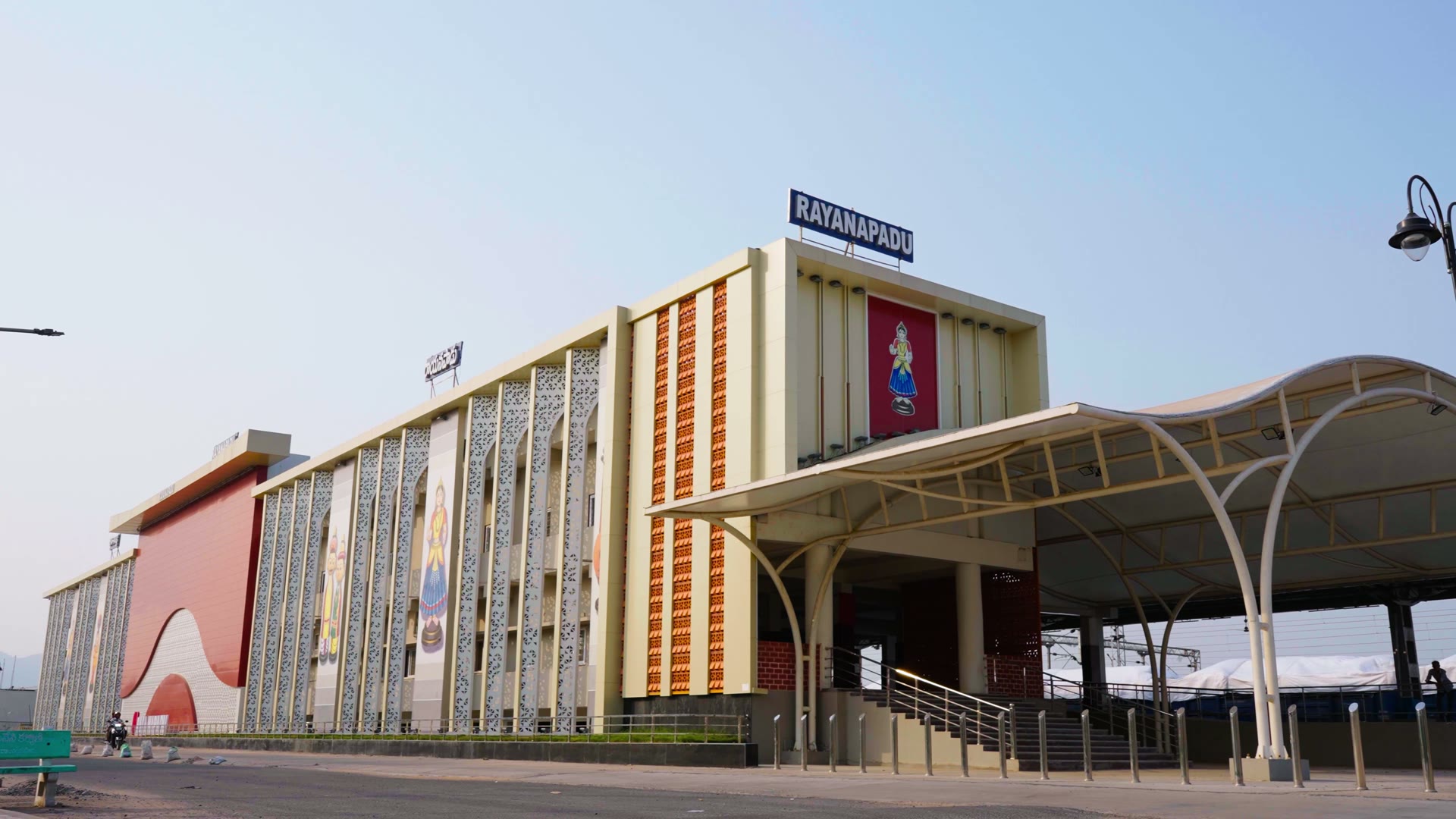 Rayanapadu station from the road: white perforated arched fins, Kondapalli toy figures, the name board and the curved canopy